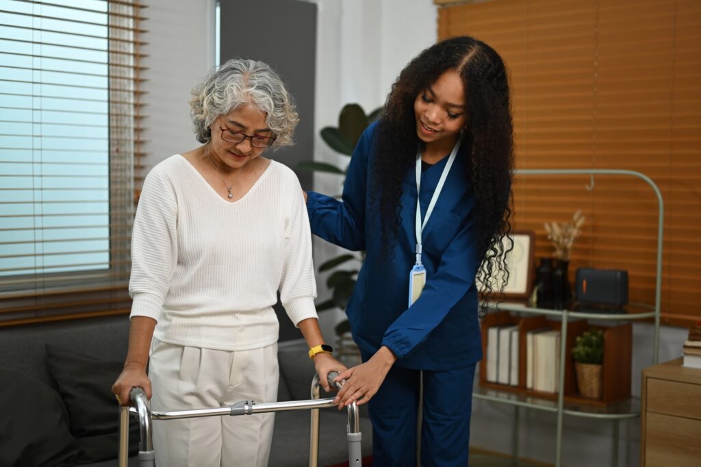 Young female caregiver is teaching senior woman to walk with walker.